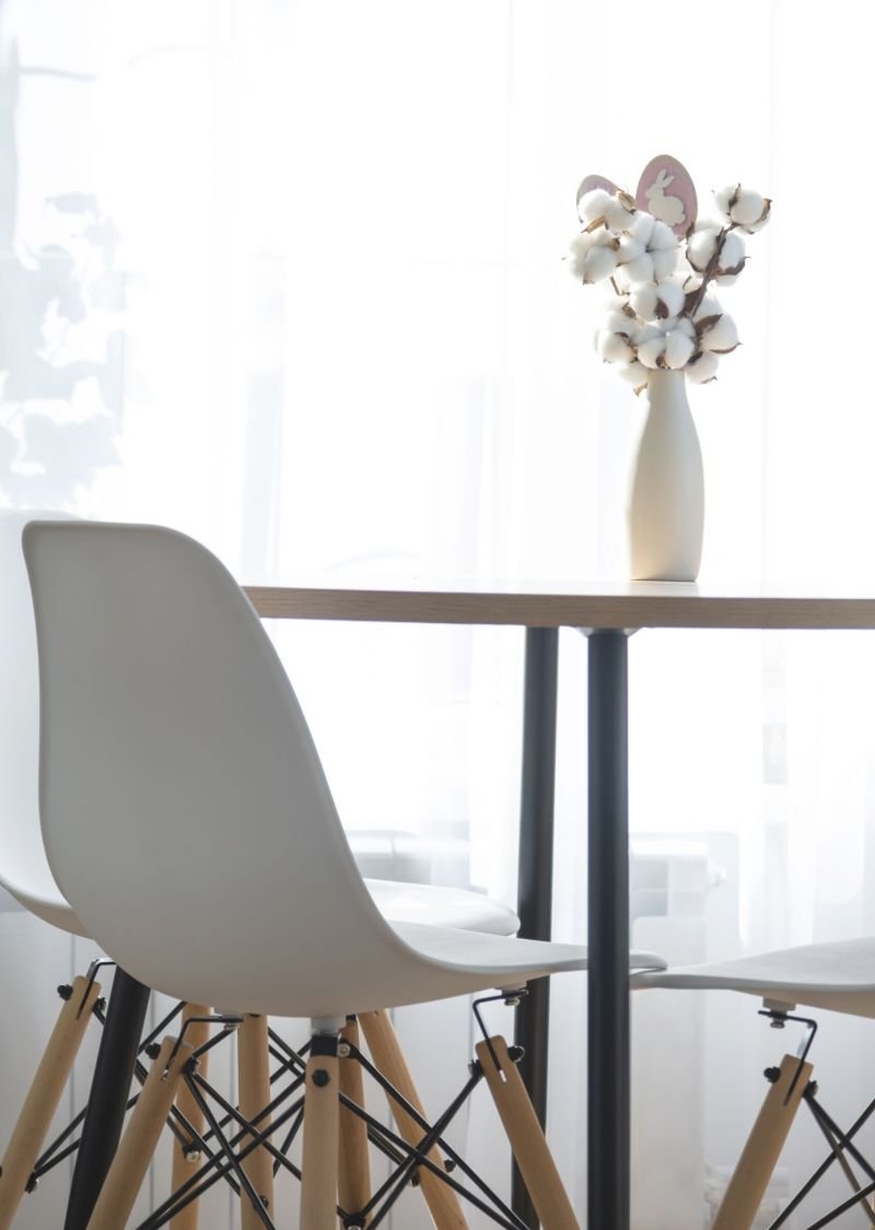 A bouquet of cotton twigs in a vase on a round table with an Easter decor of eggs and an Easter bunny in the light from the window in a minimalist interior.